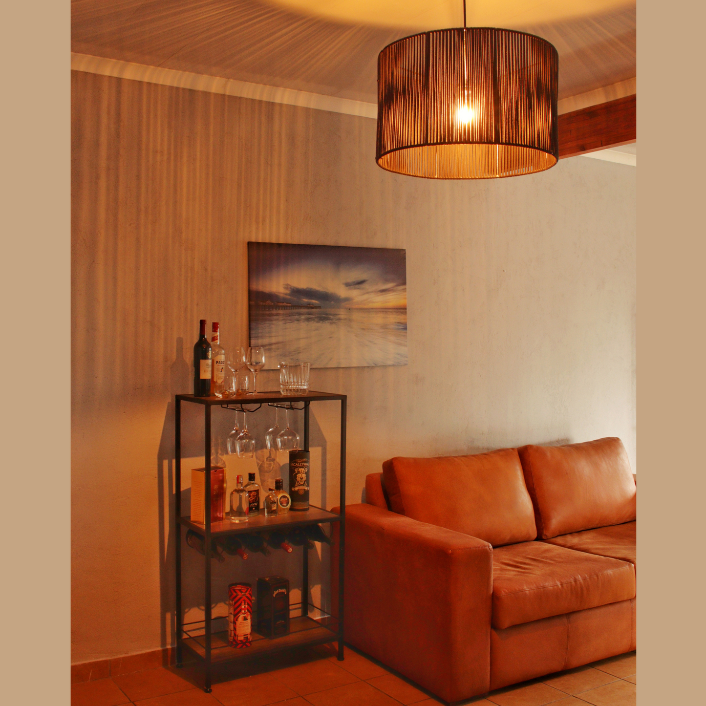 A lounge setting with a drinks unit and brown leather couch. A black pendant illuminates the area with light streaks