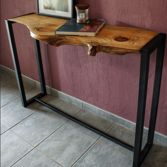 Wooden console table with black metal legs against a pink wall.