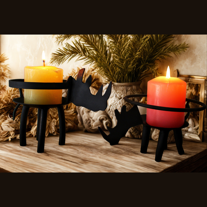 Two black rhino-shaped candle holders on a wooden surface, each holding a lit pillar candle, with a potted plant and decorative background elements behind them.