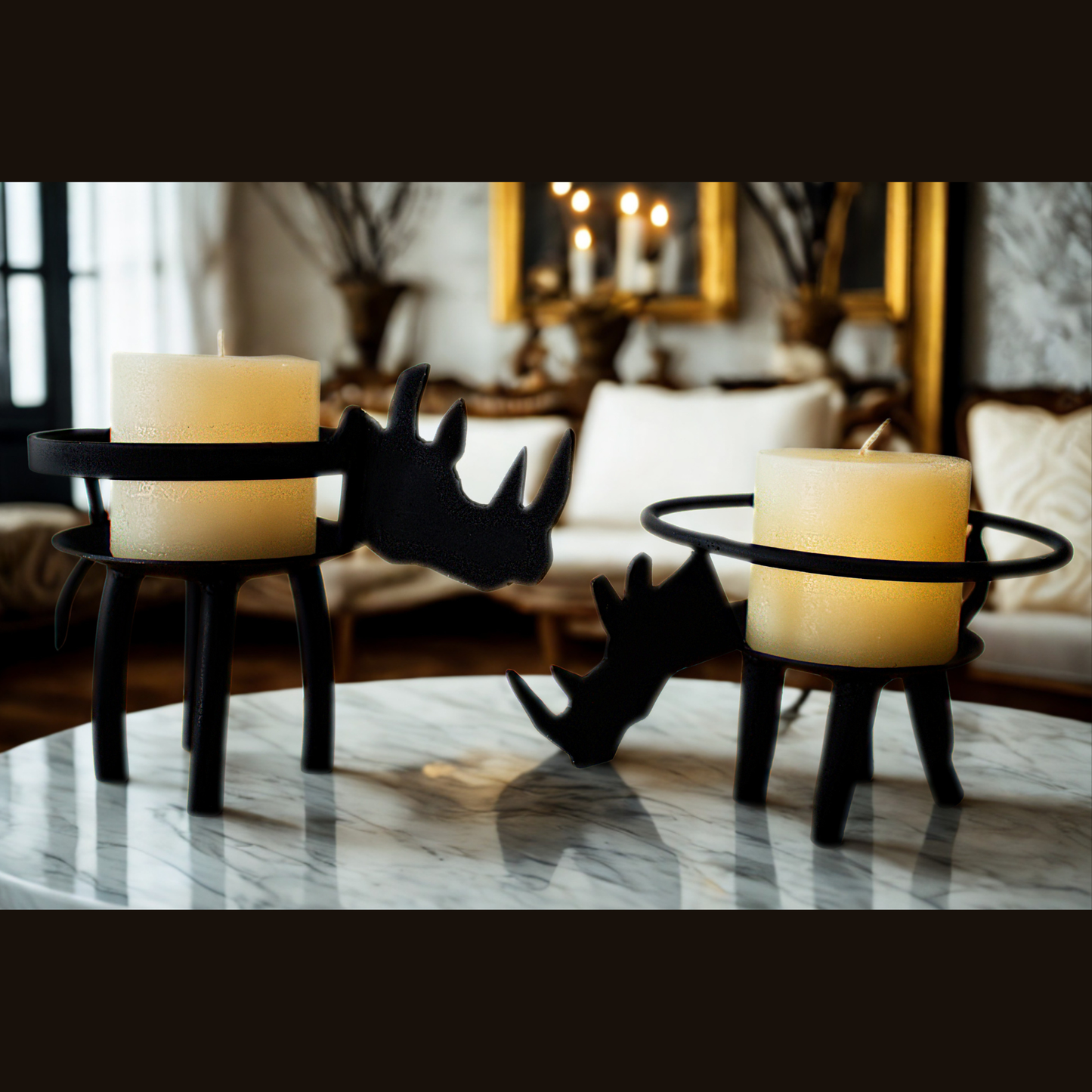 Two black metal candle holders shaped like African rhinos, each holding a lit cream pillar candle, displayed on a white marble table in a softly blurred living room setting.