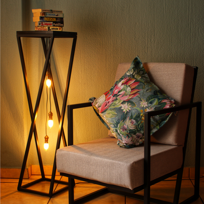 A black pendant light table with a wooden top placed next to a chair with a floral cushion, providing a warm illumination.