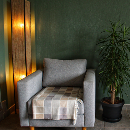 Gray armchair with a plaid blanket against a green wall with a plant on the right and modern floor lamp on the left