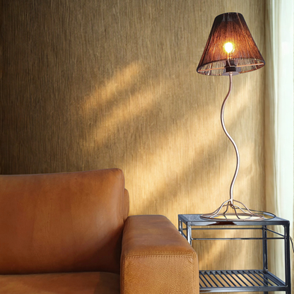 Tall table lamp on a metal side table next to a brown leather couch in front of a textured wall