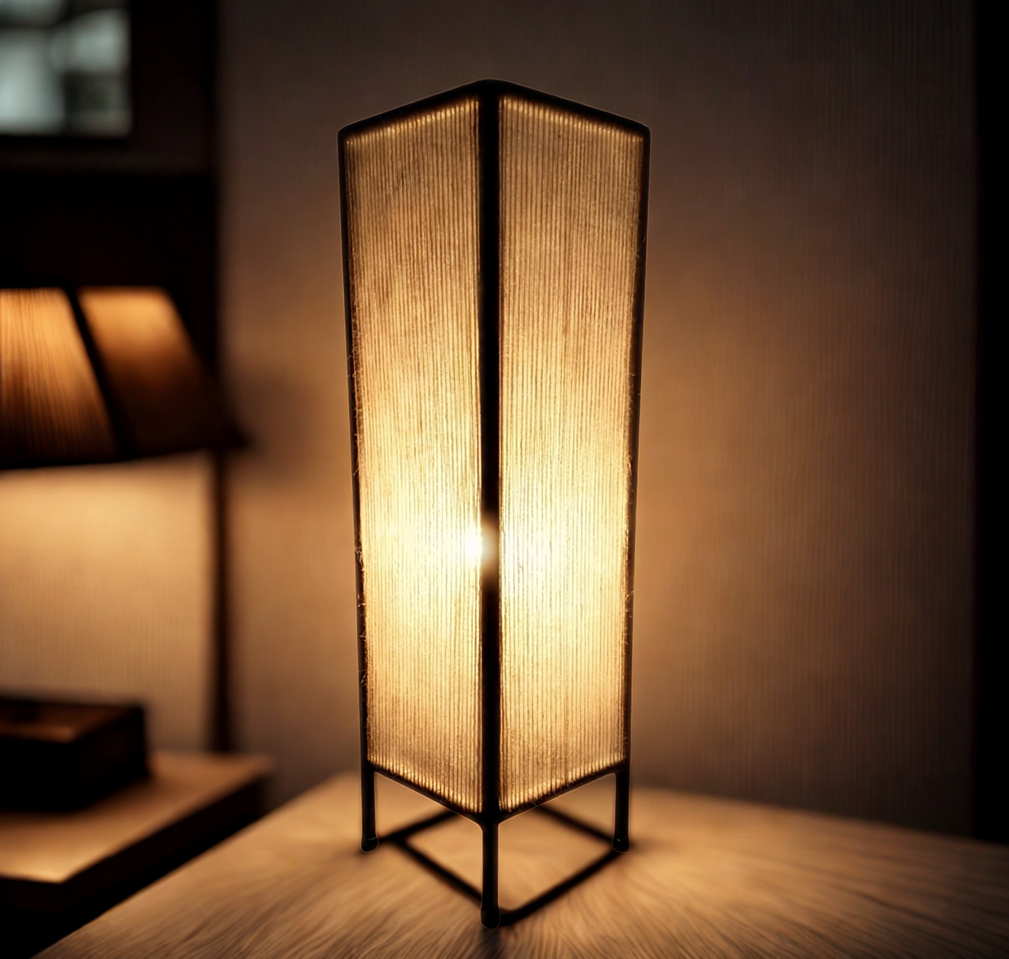 A tall rectangular floor lamp with a glowing warm light and a dark metal frame, standing on a wooden surface in a dimly lit room.