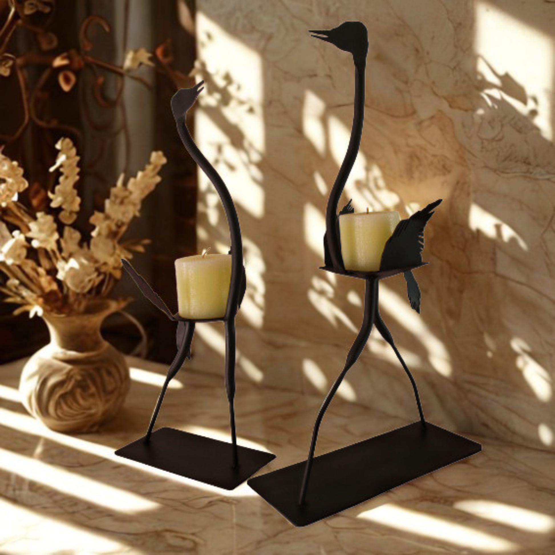 Two black metal ostrich candle holders with candles, styled on a marble surface next to a vase of dried flowers in warm, sunlit shadows.