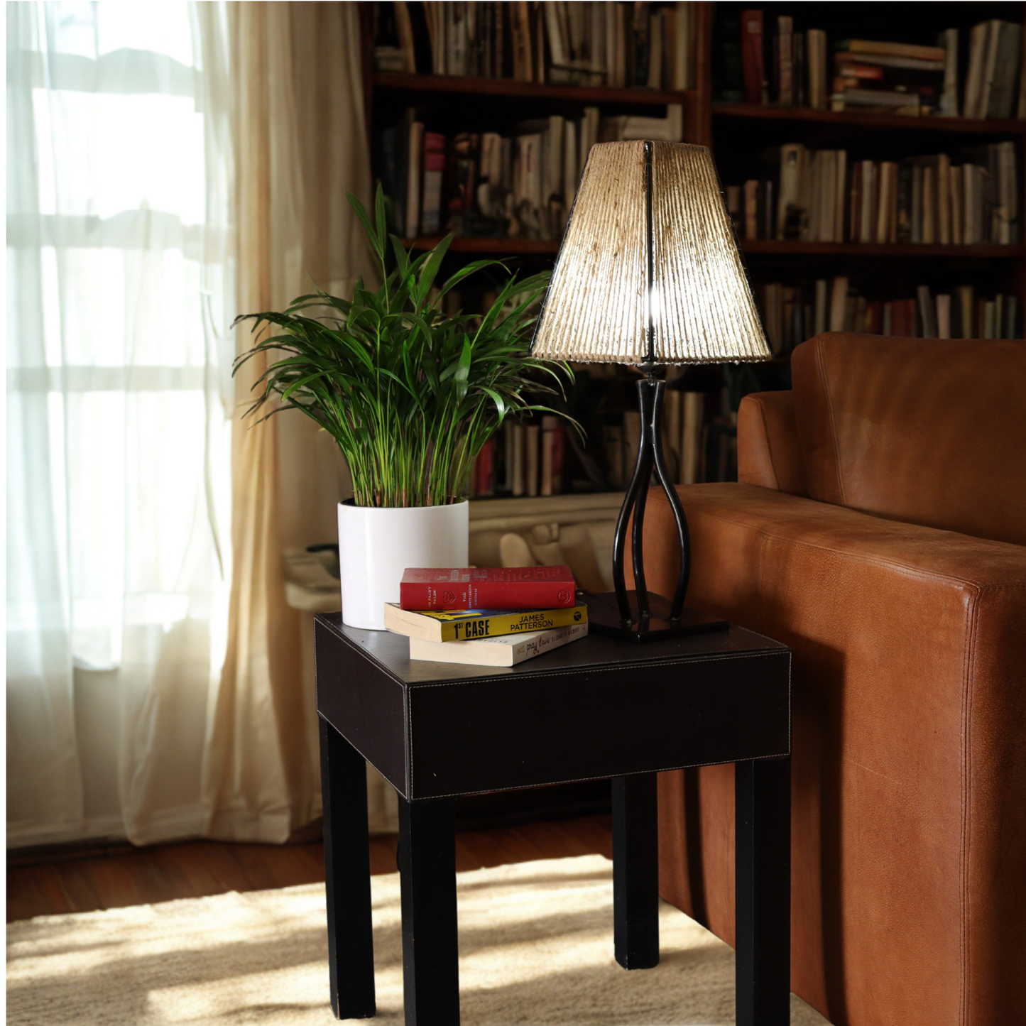 Livingroom image with a bookshelf. Side lamp on a table next to a light brown leather couch.