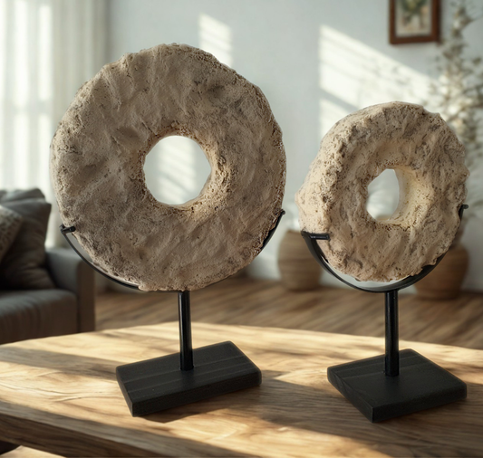 Two textured stone rong-shaped decorative sculptures displayed on black metal stands on a wooden table in a sunlit living room.